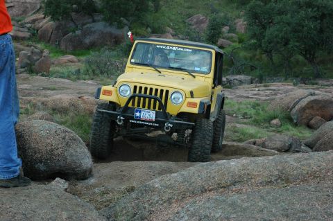2001 Jeep Wrangler - A yellow Jeep Wrangler navigates a rocky terrain, displaying a Texas license plate and a website sticker on its bumper.