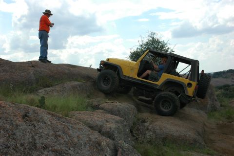 2001 Jeep Wrangler - A yellow 2001 Jeep Wrangler navigates a challenging rocky terrain under a cloudy sky.
