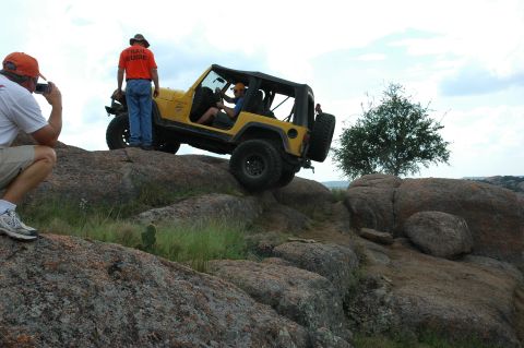 2001 Jeep Wrangler - A yellow 2001 Jeep Wrangler navigates a challenging rocky terrain, with a photographer capturing the moment.