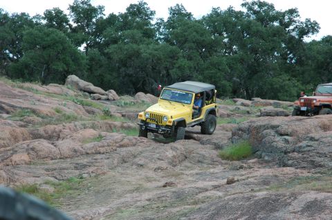 2001 Jeep Wrangler - Two Jeeps off-roading on a rocky landscape with trees in the background.