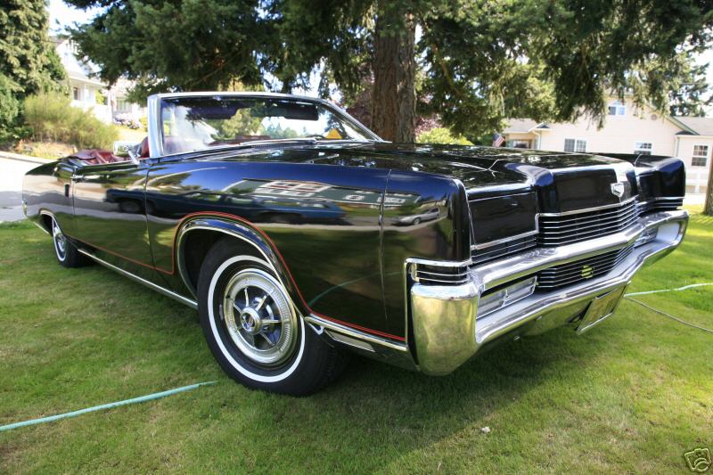 Black convertible with red interior and whitewall tires parked on grass, front three-quarter view
