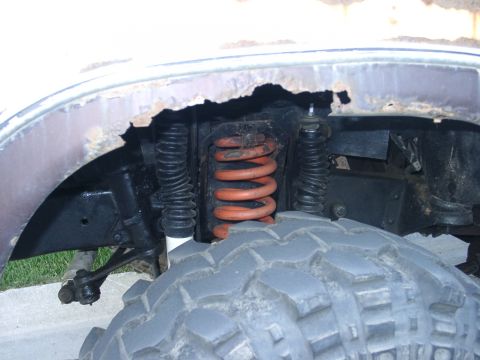 1978 Ford Bronco - Close-up of the front suspension and tire of a 1978 Ford Bronco, showing the orange coil spring and a portion of the wheel well.