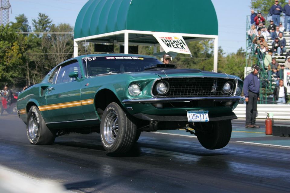 Green 1969 Ford Mustang drag car with yellow stripe, front wheels off the ground during a race