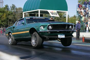 1969 Ford Mustang - A green 1969 Ford Mustang is captured mid-race with its front wheels off the ground.
