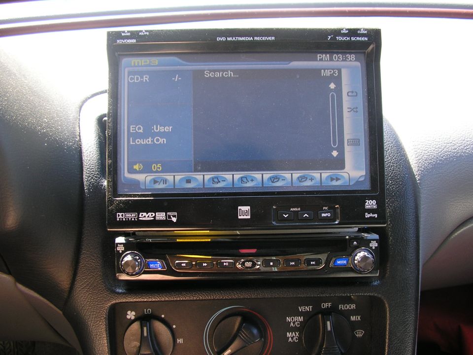 Car dashboard showing a Dual DVD multimedia receiver with a 7" touch screen displaying MP3 playback options and climate controls below