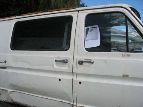 1978 Ford Bronco - A white van with visible damage to its body panels is parked outdoors, with a small photo attached to the side window.