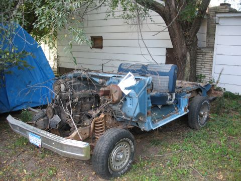 1978 Ford Bronco - This heavily weathered vehicle chassis, stripped of most of its body, sits in a yard under a tree.