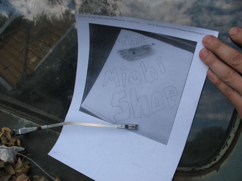 1978 Ford Bronco - A drawing on paper is placed on a car's windshield, showing a shoe and the words 'The Miobi Shop'.