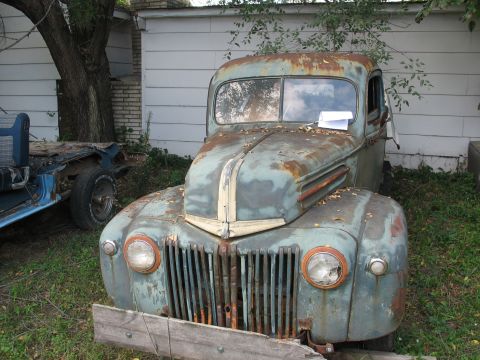 1978 Ford Bronco - A heavily rusted truck sits in a yard next to another vehicle chassis.
