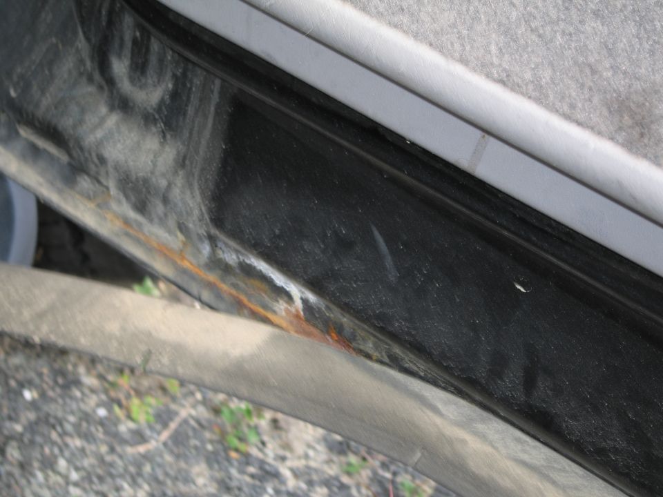 Close-up of a car's door sill showing rust and dirt