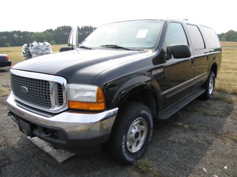 1991 Ford LTD Crown Victoria - A black Ford Excursion SUV is parked outdoors on a gravel surface with a field and trees in the background.