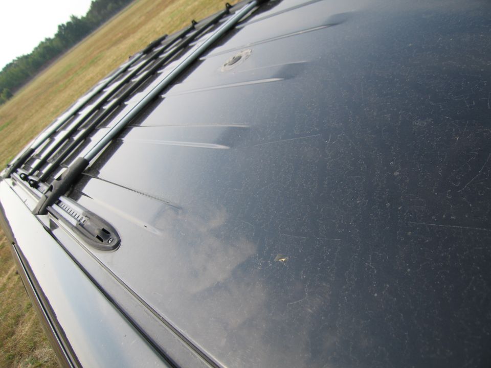 Dark vehicle roof with a roof rack, showing dust and scratches