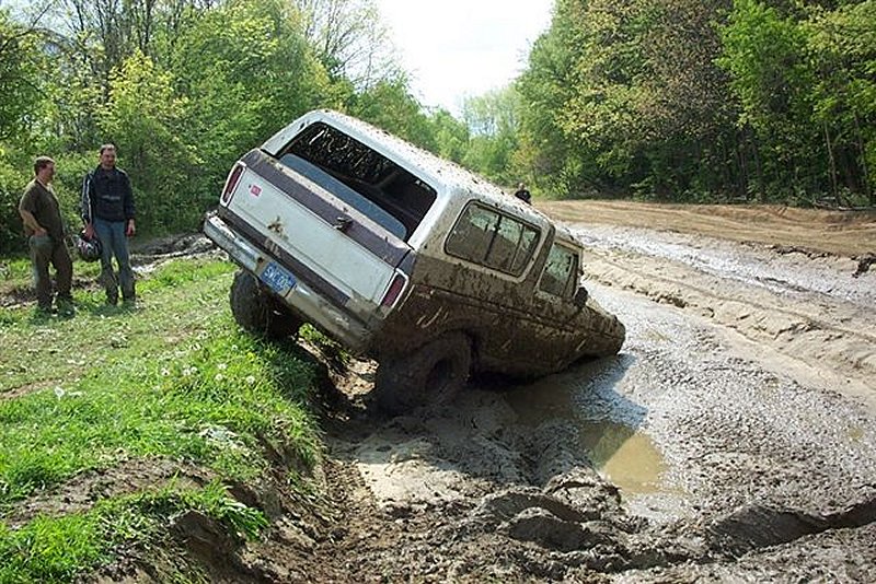 Silver full-size Bronco buried to the axles in deep mud on a rutted trail