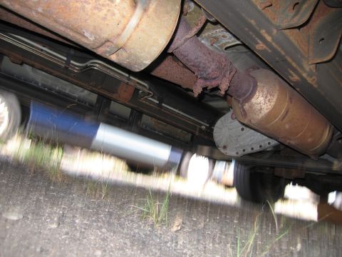 1991 Ford LTD Crown Victoria - The underside of a vehicle reveals its exhaust system, fuel tank, and suspension components.