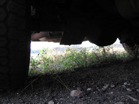 1991 Ford LTD Crown Victoria - A low-angle view of a vehicle's undercarriage, revealing its mechanical components and a grassy field in the background.