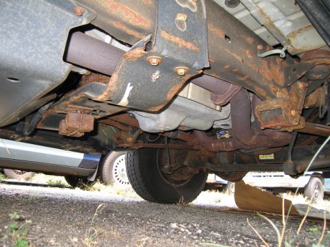 1991 Ford LTD Crown Victoria - The underside of a heavily rusted vehicle, showing the frame and exhaust components, with another vehicle partially visible.