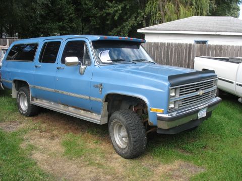 1978 Ford Bronco - This blue Chevrolet Suburban is parked next to a white pickup truck.