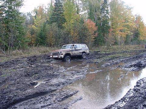 1978 Ford Bronco - A brown 1978 Ford Bronco navigates a muddy track with trees in the background.