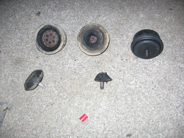 Five engine mounts on a concrete surface. Three are cylindrical with metal bases, two are conical with threaded studs