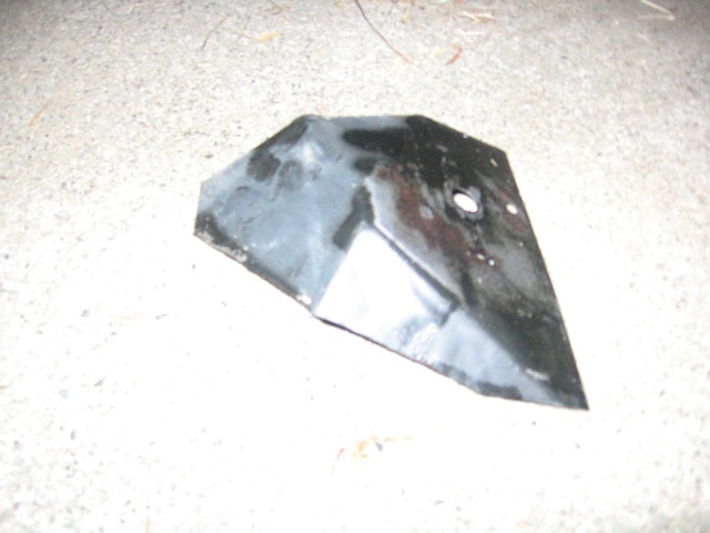 Black metal bracket with a hole, lying on a concrete surface