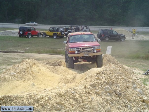 Red SUV driving over a dirt pile, with other Jeeps and SUVs in the background