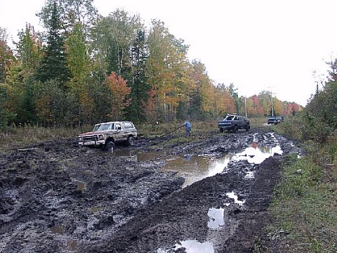 1978 Ford Bronco - Two trucks and a Ford Bronco are stuck in the mud on a trail during autumn.