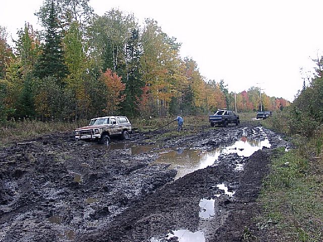 1978 Ford Bronco stuck in deep mud on a trail, another truck visible in background