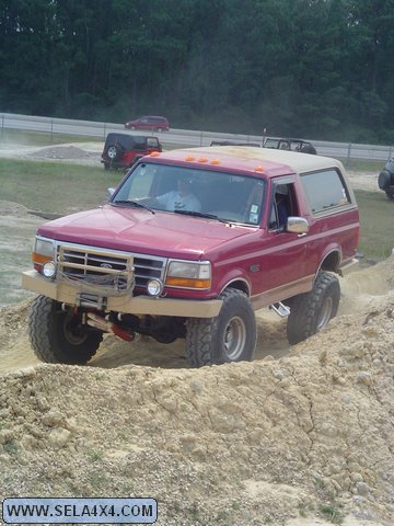 1995 Ford Bronco - This lifted 1995 Ford Bronco navigates a dirt obstacle course with other vehicles visible in the background.