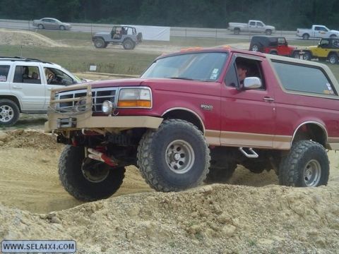 1995 Ford Bronco - Modified 1995 Ford Bronco tackles an off-road course with other vehicles nearby.