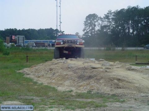 1995 Ford Bronco - A heavily modified red truck navigates an obstacle course, its front grille clearly visible.