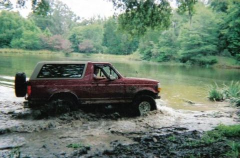 1995 Ford Bronco - This 1995 Ford Bronco is navigating through a muddy water crossing surrounded by trees.