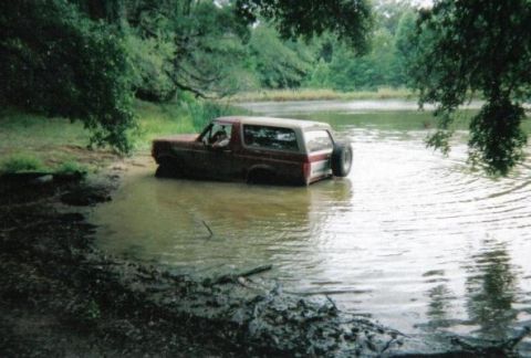 1995 Ford Bronco - A red Ford Bronco is stuck in a body of water with trees in the background.