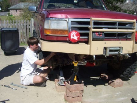 1995 Ford Bronco - A man works on the underside of a red 1995 Ford Bronco, which features a tan bull bar and winch on the front.