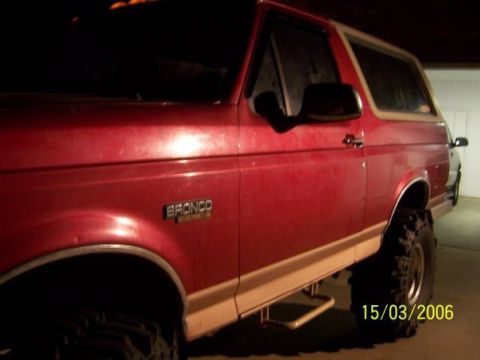 1995 Ford Bronco - Side profile of a red 1995 Ford Bronco, showing its running boards and large tires.