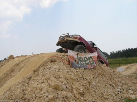 1995 Ford Bronco - A lifted maroon Ford Bronco with a tan front bumper, roof light bar and mud tires tips down the far side of a steep clay dirt mound at an o…