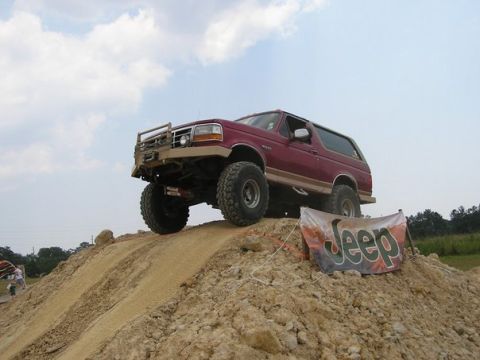 1995 Ford Bronco - A modified 1995 Ford Bronco navigates an off-road course, with a Jeep banner visible on the side of the dirt mound.