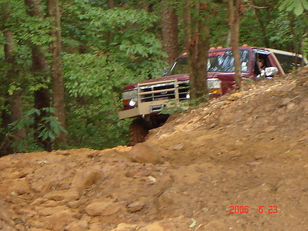 1995 Ford Bronco - Off-roading in a red pickup truck on a steep, muddy trail surrounded by trees.