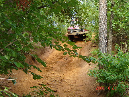 1995 Ford Bronco - A 1995 Ford Bronco navigates a steep, muddy trail through a wooded area.