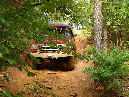 1995 Ford Bronco - Red 1995 Ford Bronco navigates an off-road trail in a wooded area.