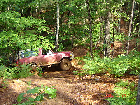 1995 Ford Bronco - A red 1995 Ford Bronco is shown off-roading through a wooded area.