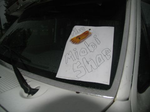 1978 Ford Bronco - A handwritten sign reading 'the Miobi Shoe' with a drawing of a foot is displayed on the windshield of a vehicle.