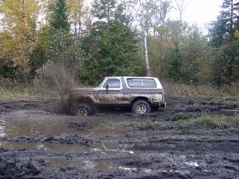1978 Ford Bronco - A 1978 Ford Bronco navigates a muddy off-road course, kicking up water and mud.