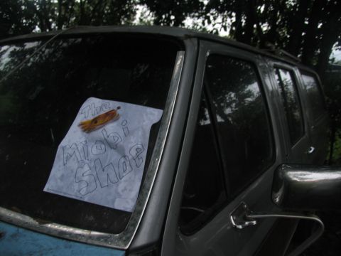 1978 Ford Bronco - A sign is placed on the windshield of a weathered SUV, with trees in the background.