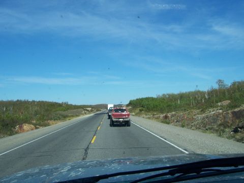 1996 Ford Bronco - A red pickup truck is seen from behind on a highway under a clear blue sky.
