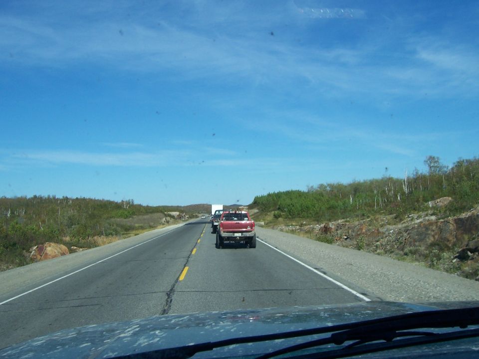 Red pickup truck driving on a highway with a white truck behind it