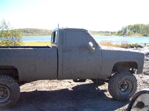 1996 Ford Bronco - Mud-covered pickup truck parked near a body of water on a sunny day.
