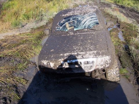 1996 Ford Bronco - This vehicle is completely covered in mud and stuck in a muddy area, with only the front visible.