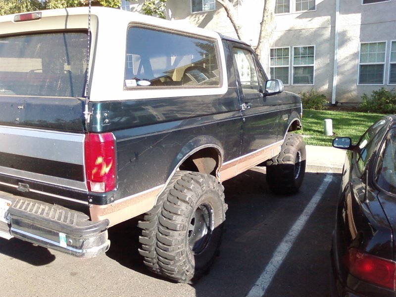 Dark green and white Ford Bronco with large off-road tires parked in a lot