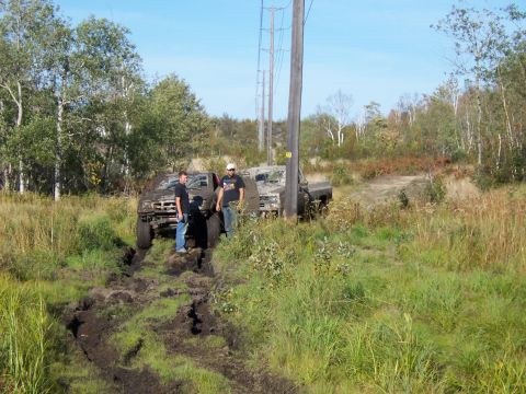 1996 Ford Bronco - Two trucks are stuck in a muddy off-road trail with two men observing the situation.