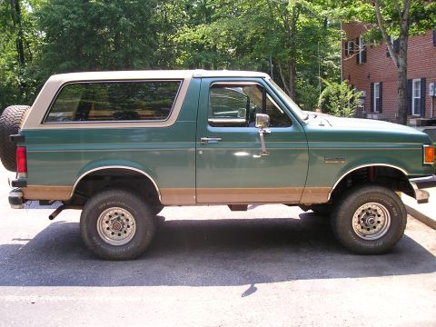 1989 Ford Bronco - This 1989 Ford Bronco is parked outdoors with trees and a brick building in the background.